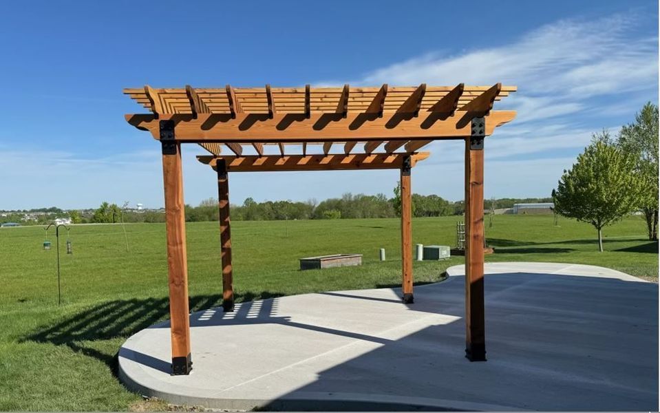 A wooden pergola is in the middle of a grassy field