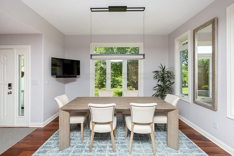 A dining room with a table and chairs and a television on the wall.