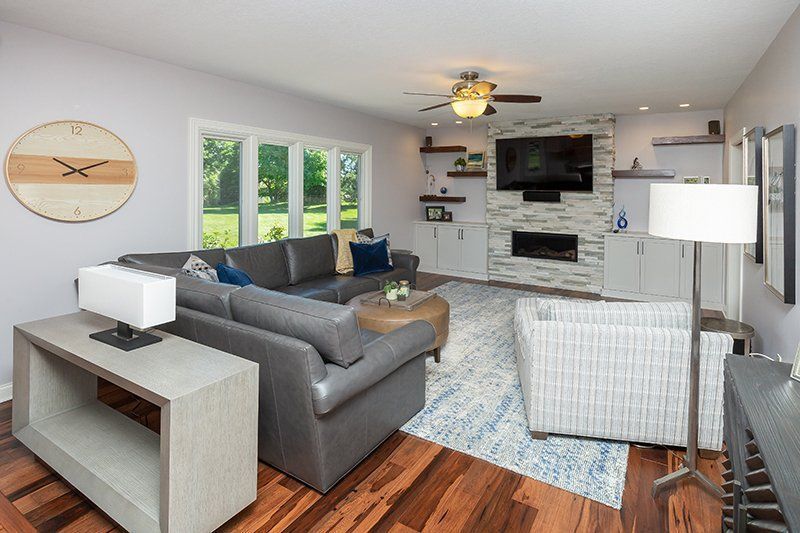 A living room with a couch , chairs , a fireplace and a clock on the wall.