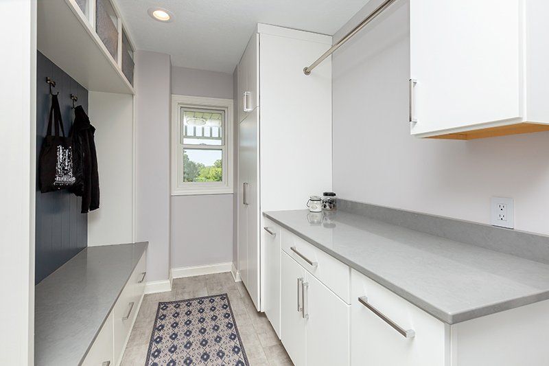 A laundry room with white cabinets and a window.
