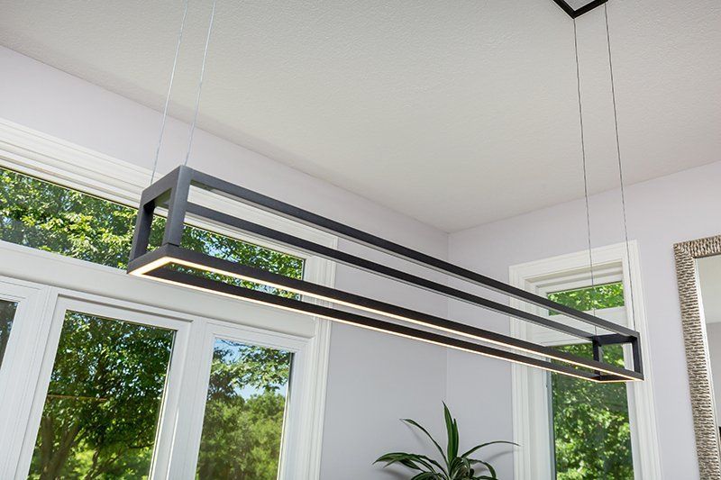 A long light fixture is hanging from the ceiling in a room next to a window.