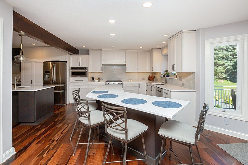 A kitchen with hardwood floors , white cabinets and stainless steel appliances.