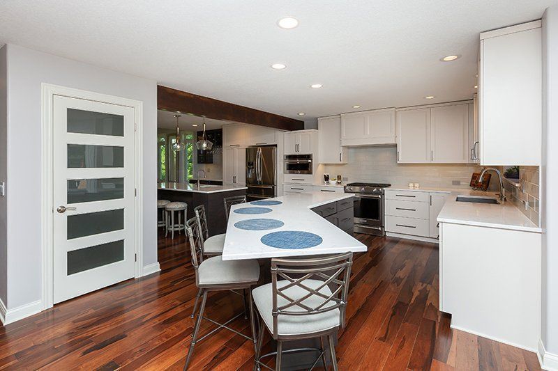A kitchen with hardwood floors , white cabinets , a table and chairs.