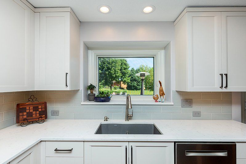 A kitchen with white cabinets , a sink , and a window.