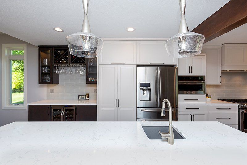 A kitchen with white cabinets , stainless steel appliances , a sink and a refrigerator.