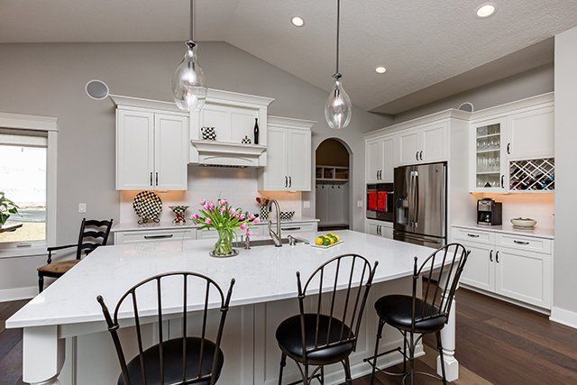 A kitchen with white cabinets and black chairs and a large island.