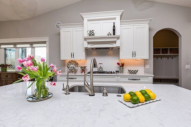 A kitchen with white cabinets , a sink , and a vase of flowers on the counter.