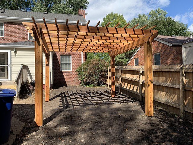 A wooden pergola is in the backyard of a house.