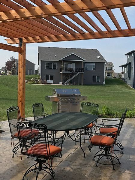 A table and chairs under a pergola with a house in the background
