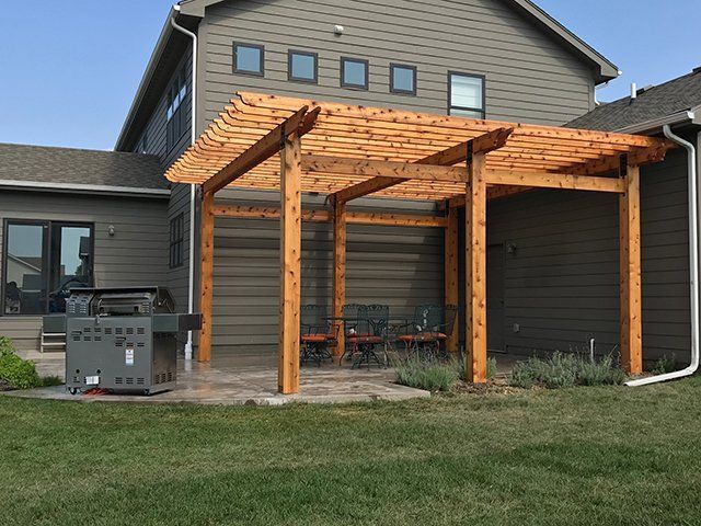 A wooden pergola is in the backyard of a house.