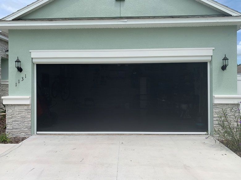 A green house with a black garage door with a screen on it.