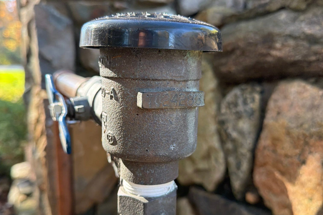 Close-up of a metal water valve with a black cap against a stone wall.