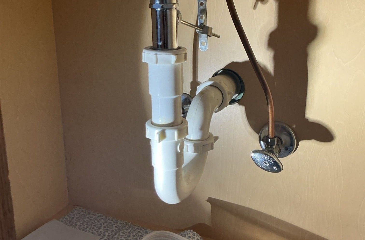 Under-sink plumbing with white P-trap and shutoff valve inside a cabinet.