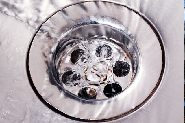 Water draining down a shiny, metallic sink drain, with bubbles forming.