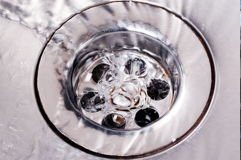 Water draining down a shiny, metallic sink drain, with bubbles forming.