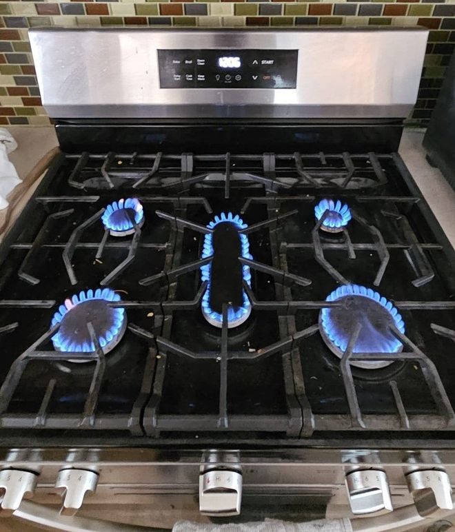 Gas stove with five blue flames lit on a black grates cooktop