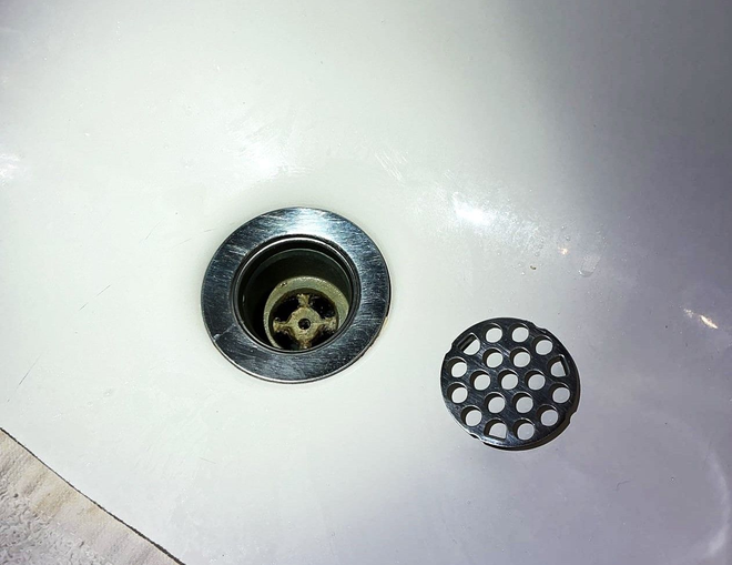 Close-up of a white sink drain with a removable round strainer beside it.