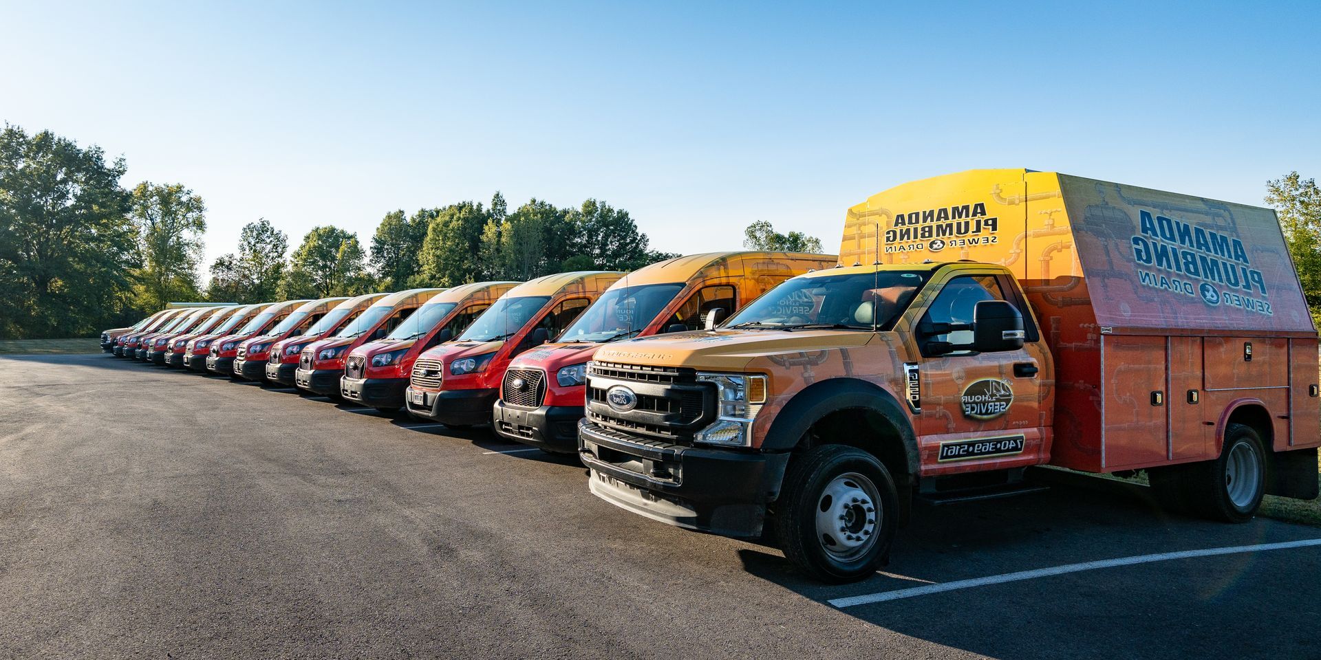 Line of orange and red vans parked on asphalt; one larger truck in front, all with company logos.