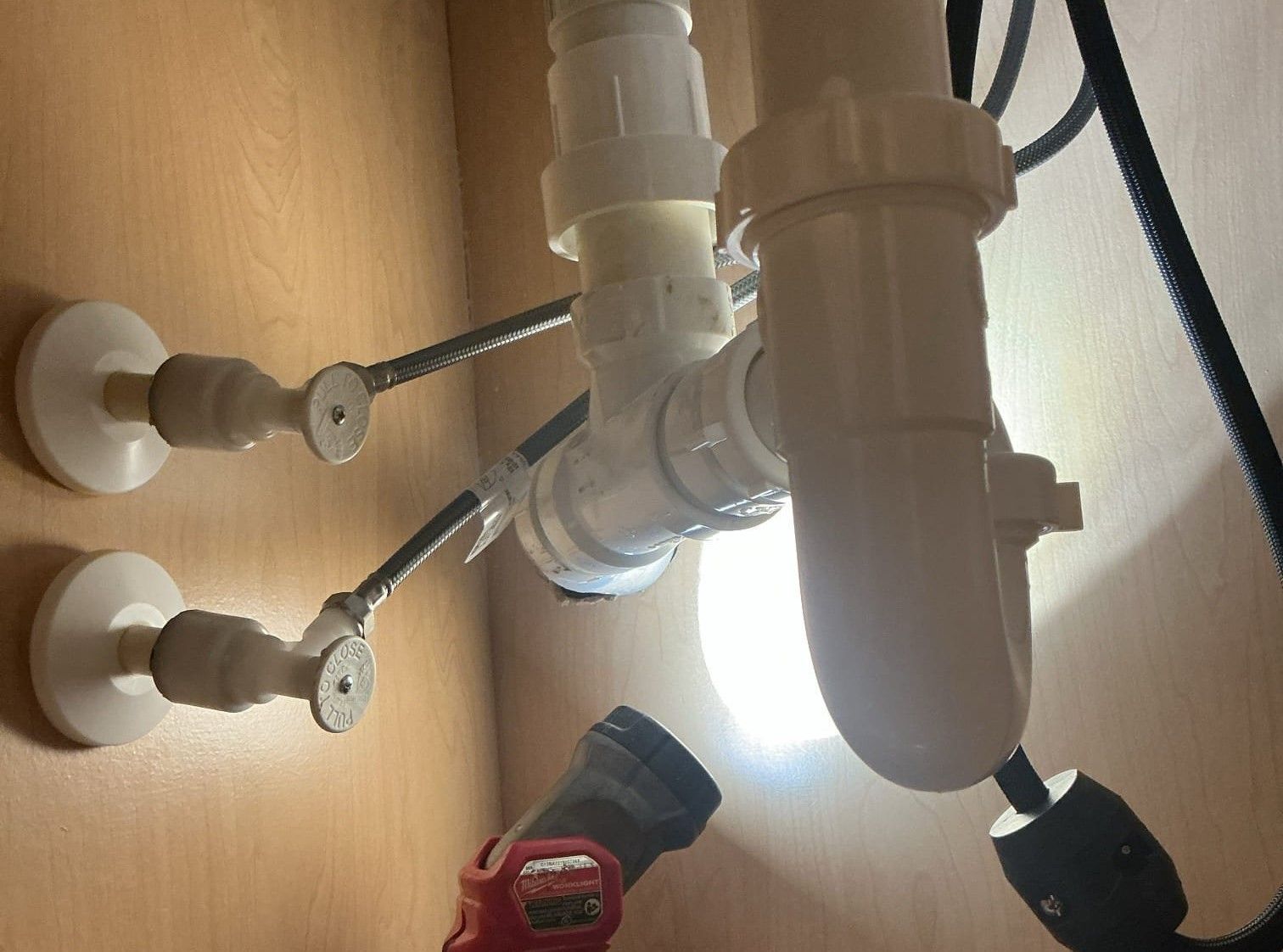 Under-sink plumbing with white pipes, shutoff valves, and a red flashlight on the cabinet floor