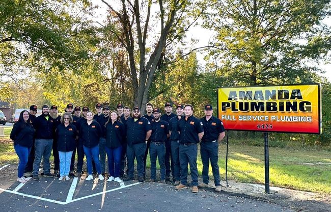 Group photo of Amanda Plumbing employees in front of a sign in a sunny outdoor setting.