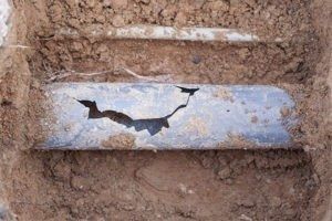 Damaged pipe with a large crack, buried in dirt.