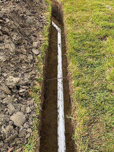 White pipe in trench dug in grass.