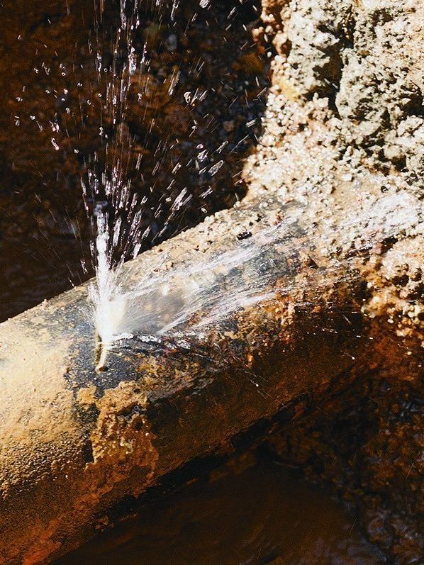 Leaking water pipe spurting water, surrounded by brown soil.