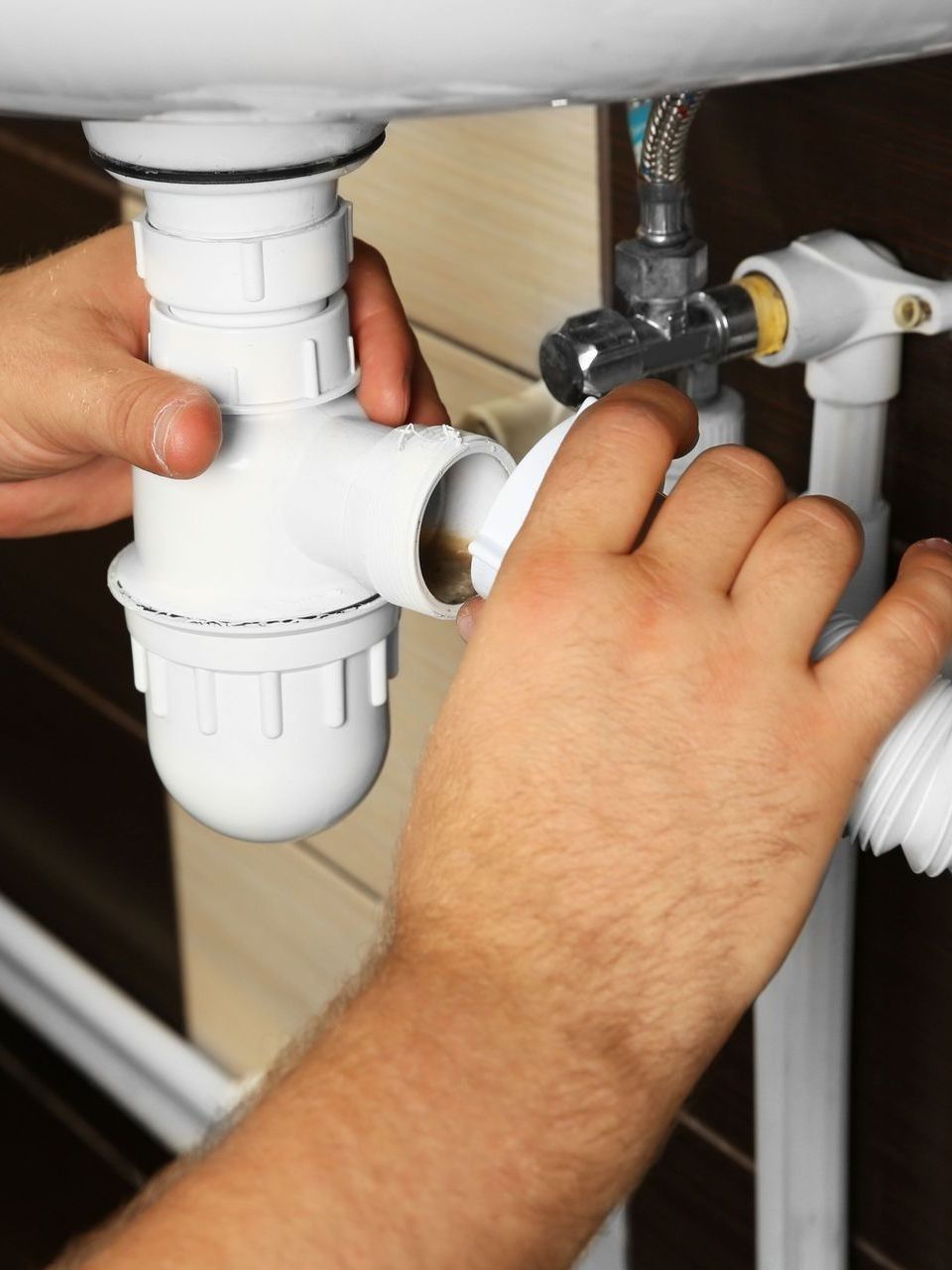 Hands assembling white plumbing under a sink.