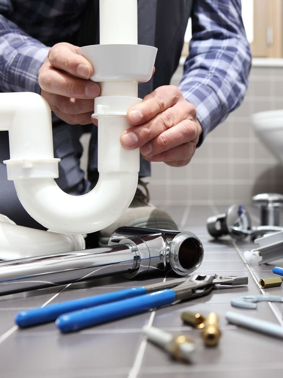 Plumber fixing a white sink drain with tools on a tile floor.