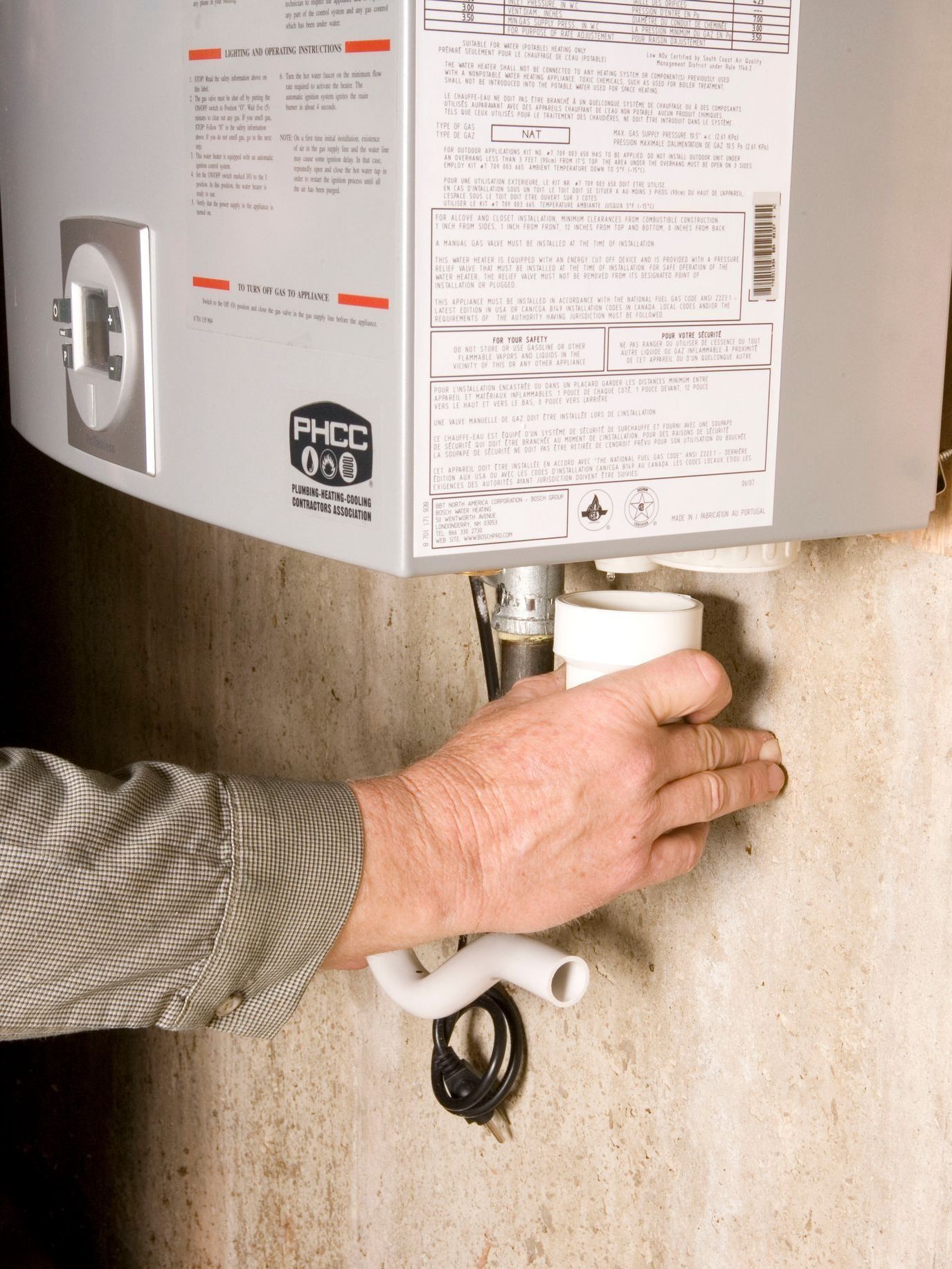 Person adjusting a white water heater drain valve in a basement.