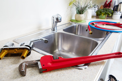 A red wrench and plumbing parts on a kitchen countertop next to a double sink.