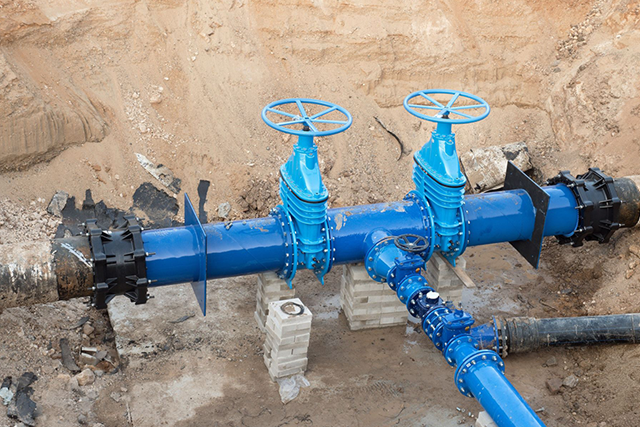 Blue water pipes with valves in a construction site, surrounded by dirt and concrete blocks.