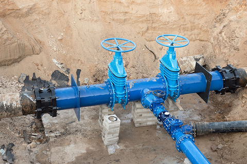 Blue water pipes with valves in a construction site, surrounded by dirt and concrete blocks.