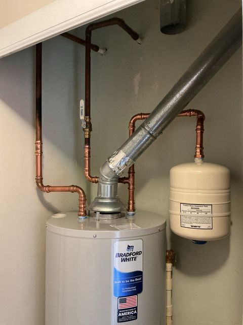 Water heater with copper pipes and a small expansion tank in a utility closet