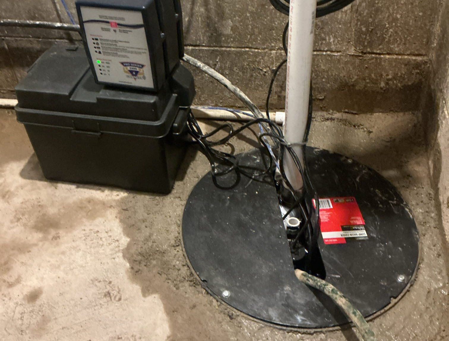 Basement utility area with pump equipment, black tank, white pipe, and coiled cable on a concrete floor.