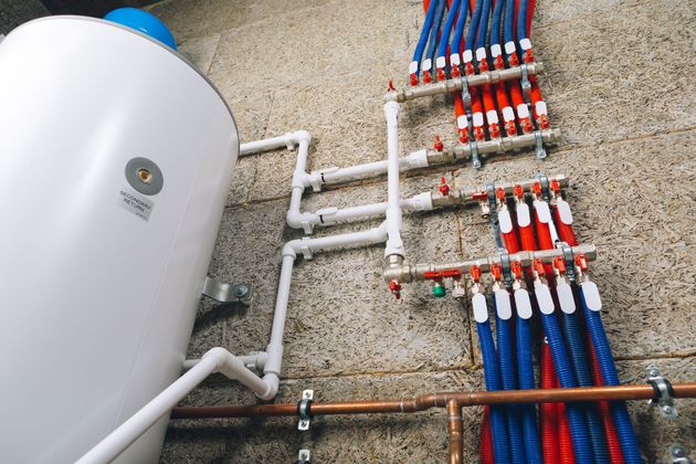 White water tank with copper and blue-red plumbing pipes on a wall in a utility room