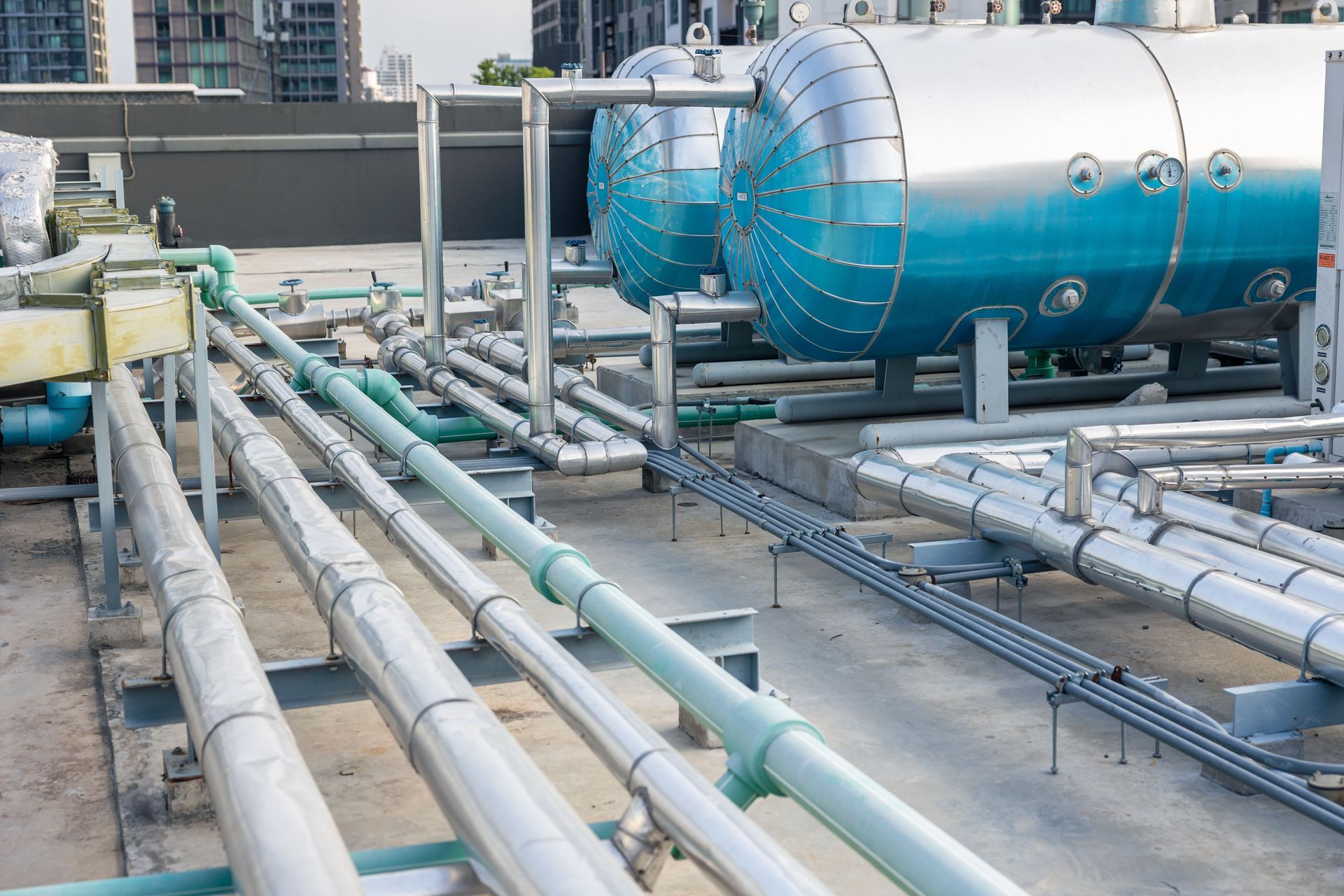 Industrial rooftop piping with large blue tanks and metal ducts on a facility roof