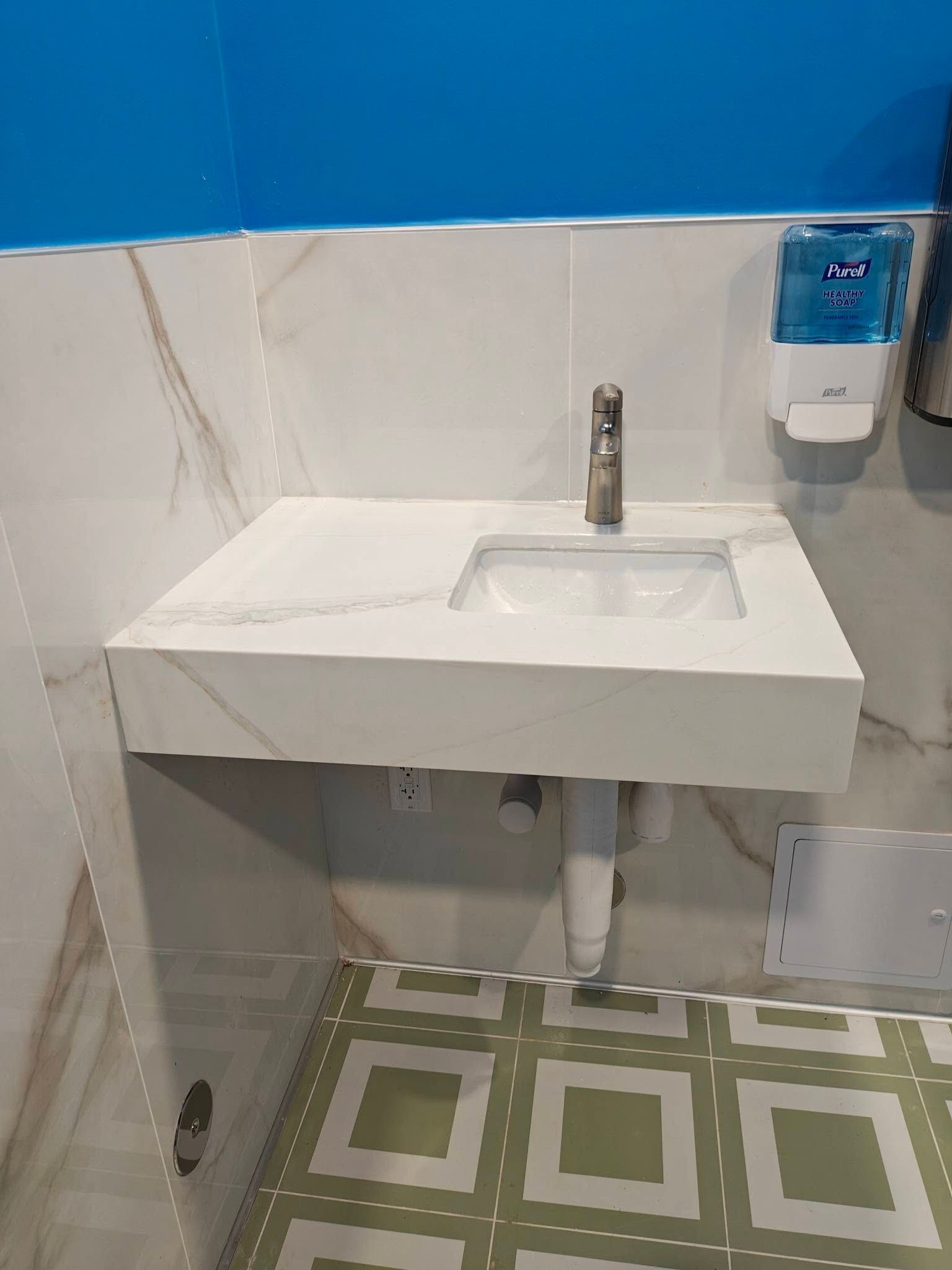 Small white sink with faucet in a tiled restroom, with blue and white walls and patterned green floor tiles.