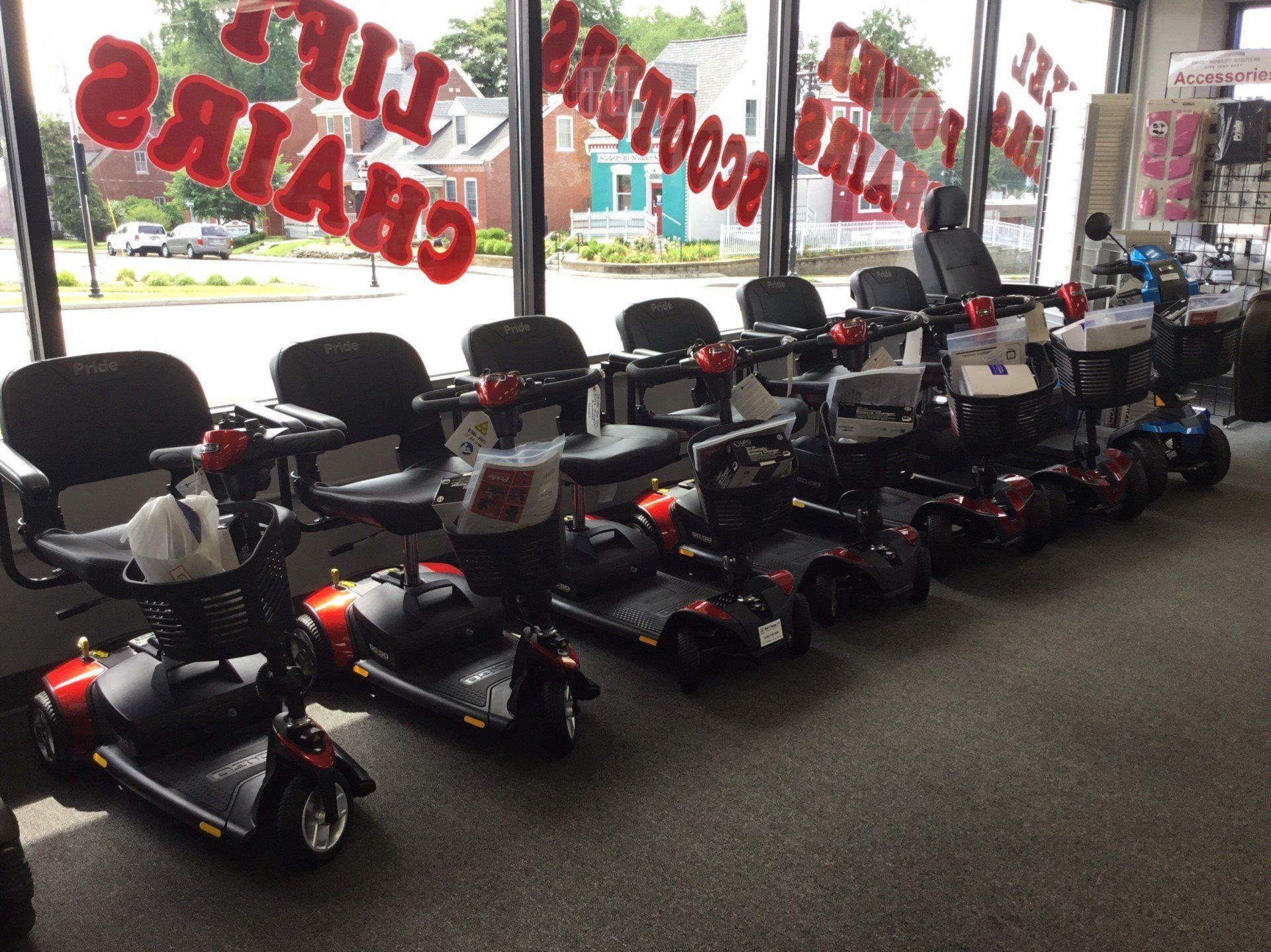 Mobility scooters in a store window; red and black scooters, chairs, signs.