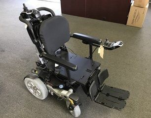 A black and gray power wheelchair with armrests and footrests, indoors.