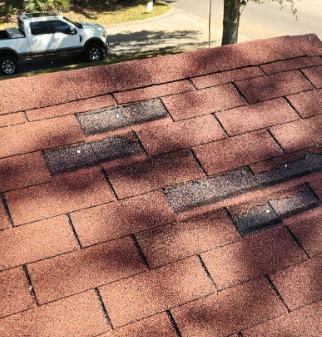 Damaged asphalt shingle roof, showing missing granules and exposed underlayment.
