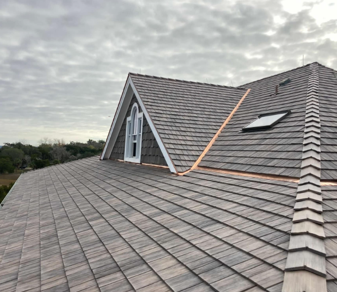 Gray cedar shingle roof with a dormer and a skylight under an overcast sky.