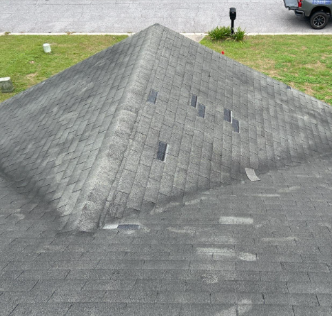 Gray asphalt shingle roof with vent stacks, on a house, viewed from above, with a street in the background.