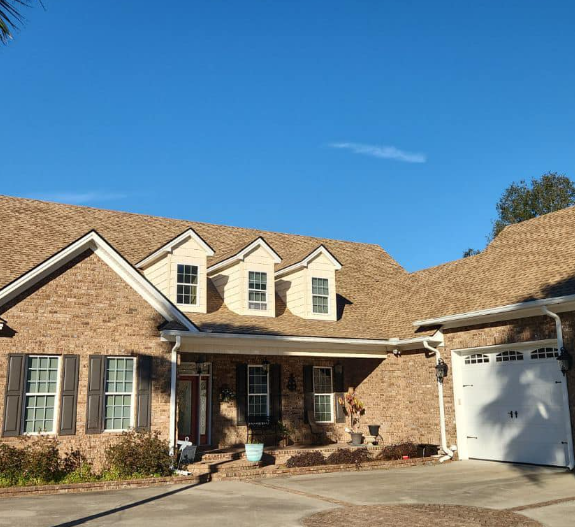 Brick house with brown roof, three dormers, and a garage on a sunny day.