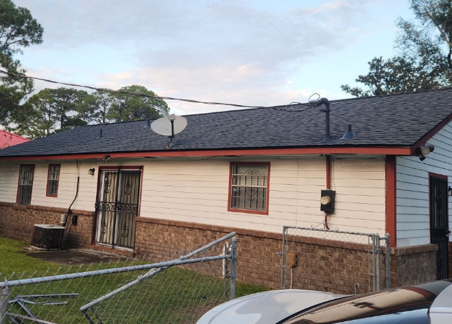 Back view of a white house with a dark roof and a brick foundation, with a satellite dish and a metal door.