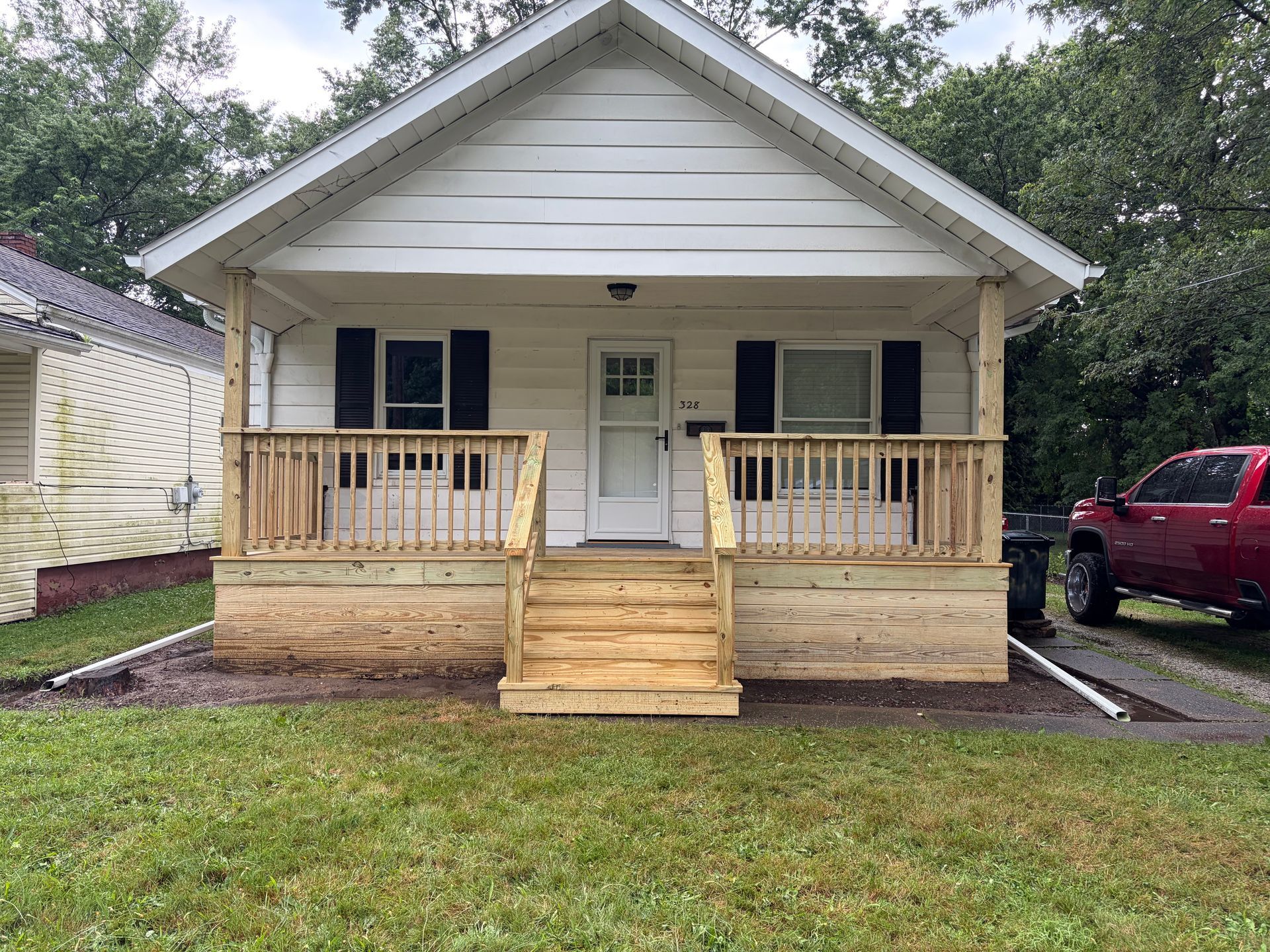 Small beige house with front porch, wooden steps, and a red truck parked to the right.
