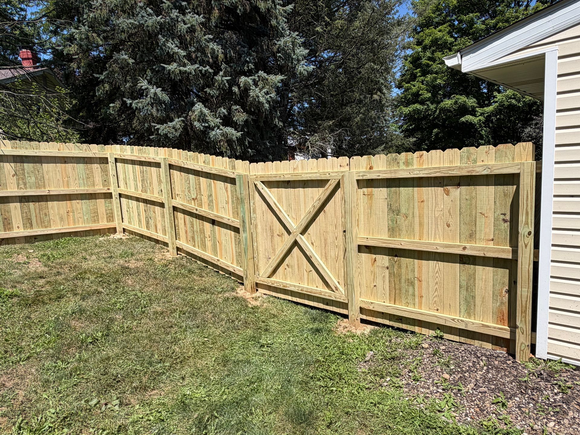 Wooden privacy fence with a gate in a grassy backyard beside a white house