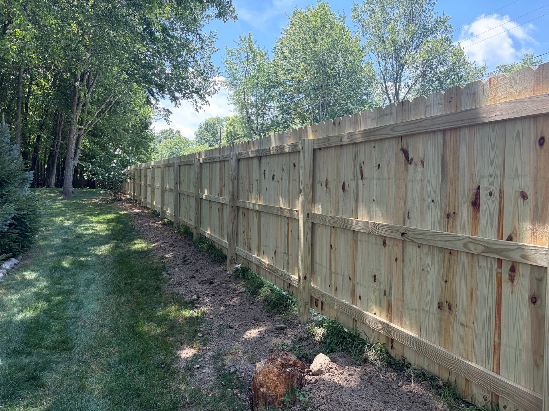 Wooden privacy fence along a grassy wooded path on a sunny day