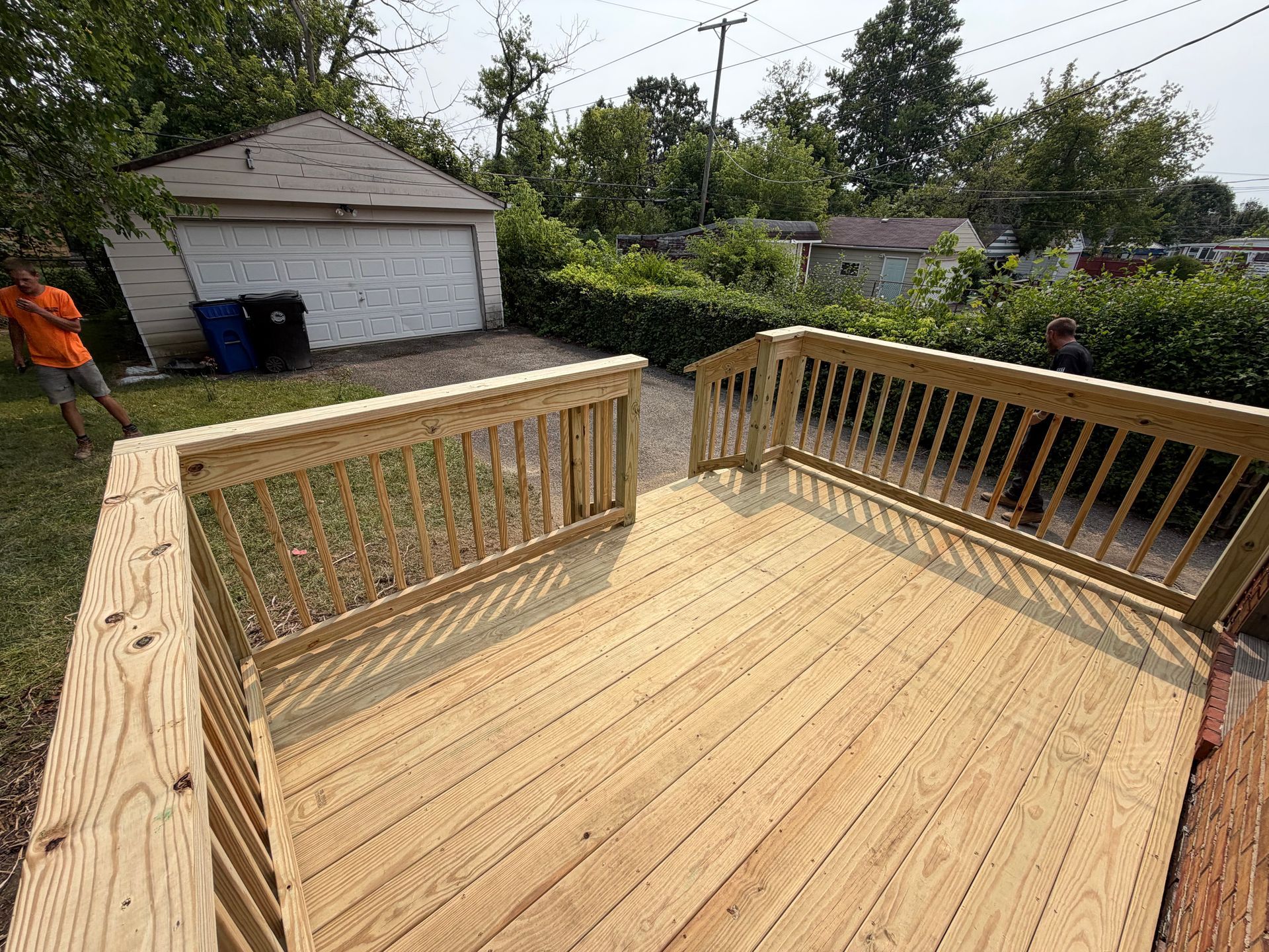 Wooden backyard deck with railings, viewed from the house, under construction beside a garage and trees.