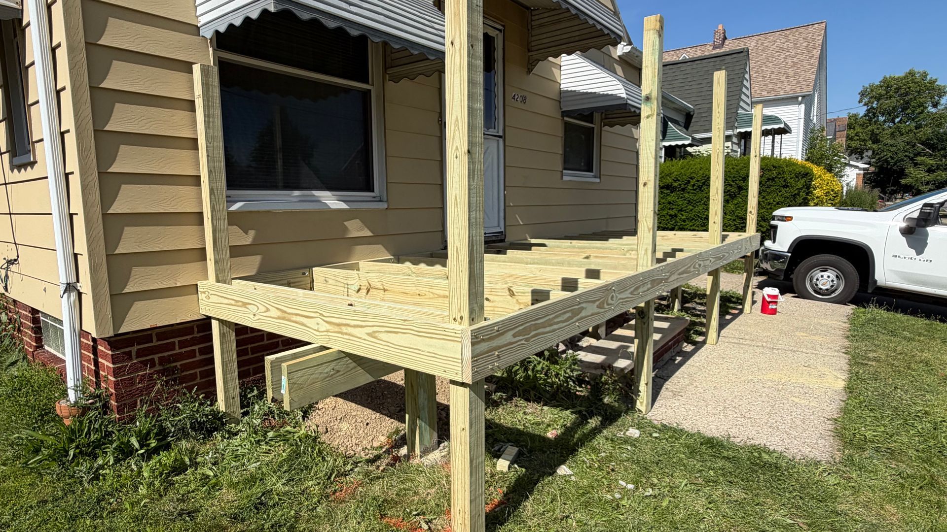 Wooden porch under construction on a tan house, with a white truck parked beside it.